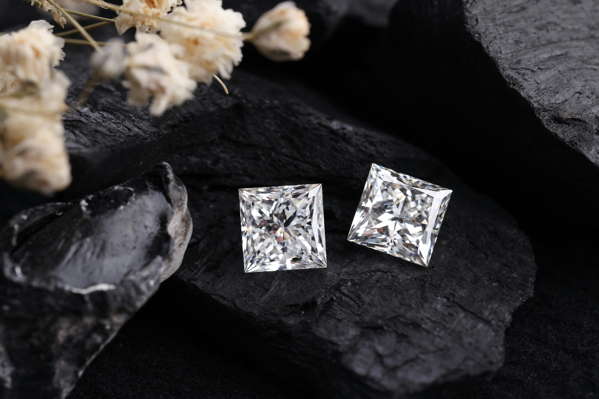 Two princess-cut natural diamonds resting on raw coal, a nod to the carbon origins of every diamond