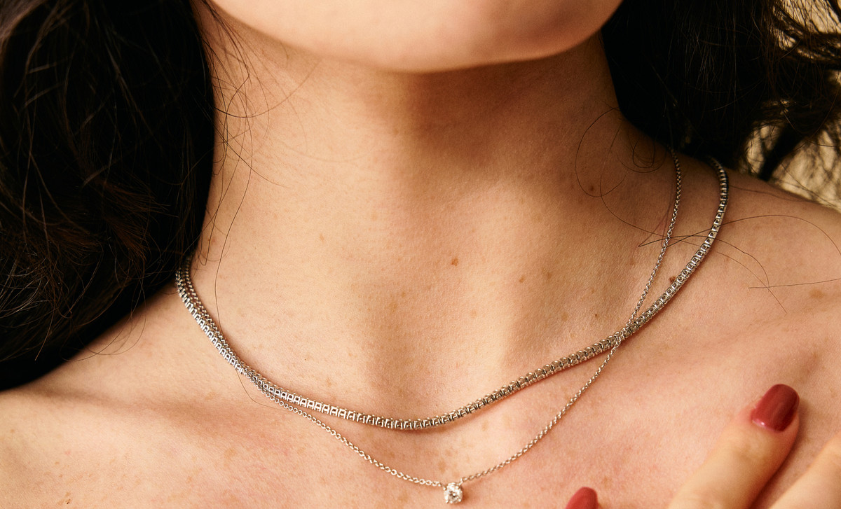 A diamond Riviera necklace worn on the collarbone, layered with a delicate solitaire pendant — handmade by MAISON IN, Antwerp